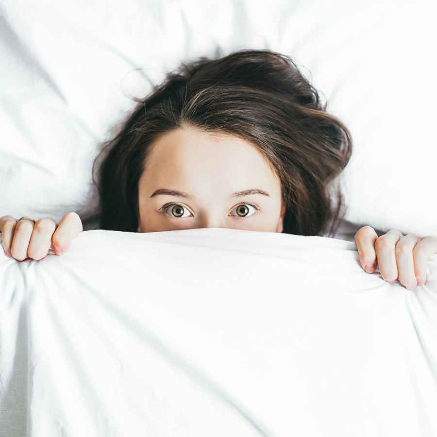 Schlafstoerungen-Ashwagandha-Kalifornischer-Mohn Frau im Bett verdeckt ihr unteres gesicht mit einer decke