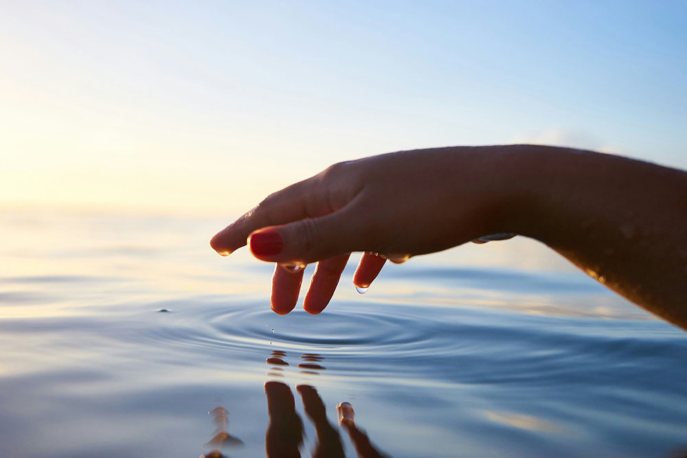 Wasser-Ruhe Hand tupft ins Meerwasser beim Sonnenuntergang